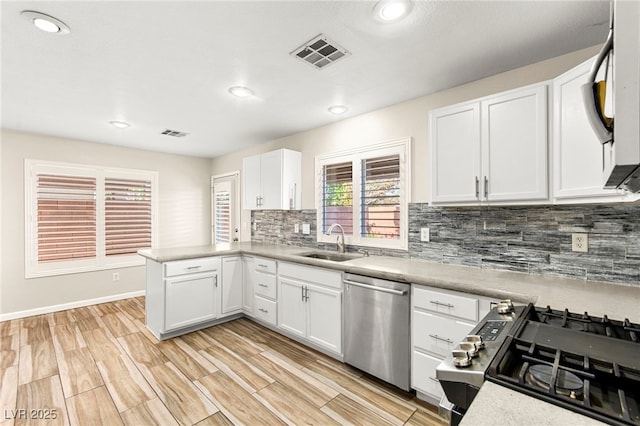 kitchen with dishwasher, a sink, decorative backsplash, a peninsula, and white cabinetry