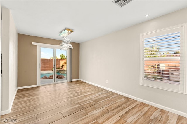 empty room with a chandelier, light wood-style flooring, and baseboards
