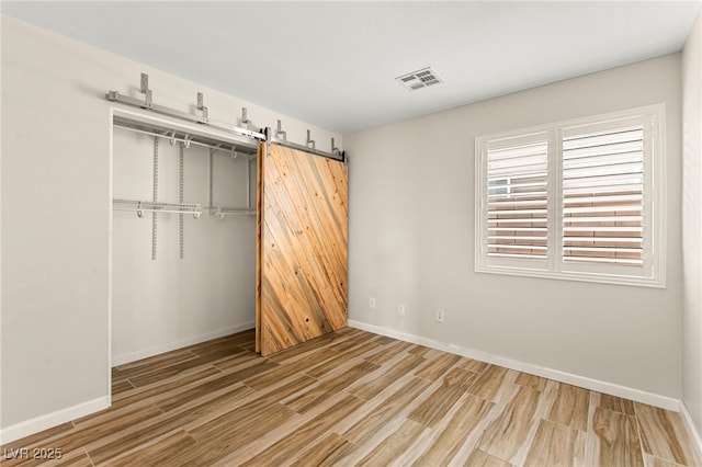 unfurnished bedroom with wood finished floors, a closet, baseboards, and a barn door