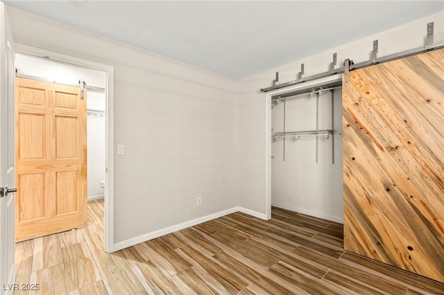 unfurnished bedroom with a barn door, wood finished floors, and baseboards