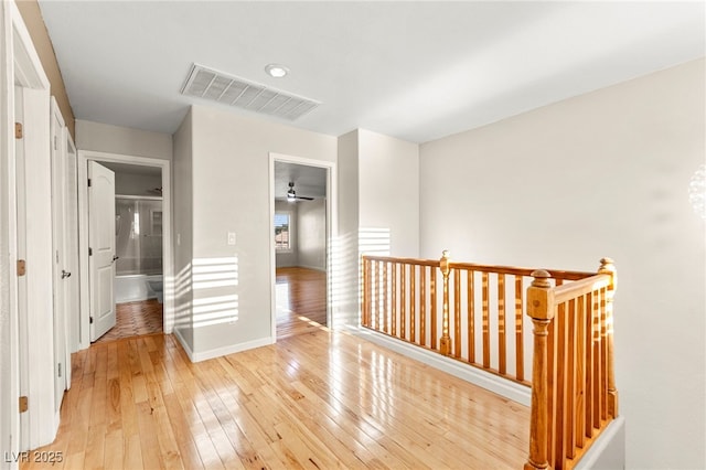 hall featuring an upstairs landing, light wood-type flooring, and baseboards