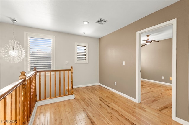 spare room featuring light wood finished floors, a chandelier, baseboards, and a ceiling fan