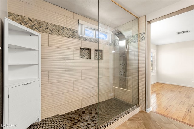 full bathroom with a tile shower, baseboards, and wood finished floors