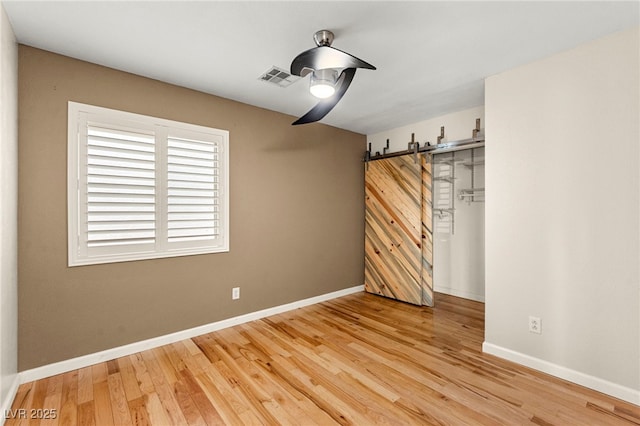 unfurnished bedroom featuring wood finished floors, a barn door, baseboards, and a ceiling fan