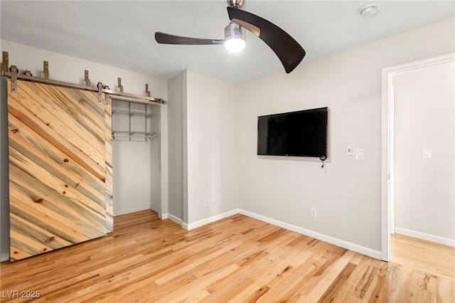 unfurnished bedroom with wood finished floors, baseboards, a closet, ceiling fan, and a barn door