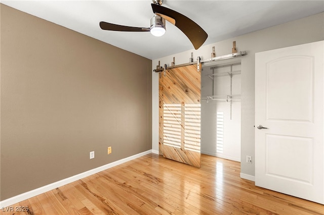 unfurnished bedroom with light wood finished floors, baseboards, ceiling fan, and a barn door