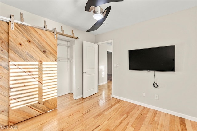 unfurnished bedroom featuring a barn door, wood finished floors, and baseboards