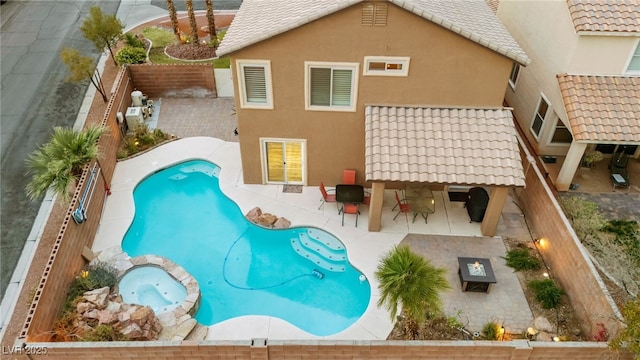 back of house featuring a pool with connected hot tub, a fenced backyard, stucco siding, a patio area, and a tiled roof