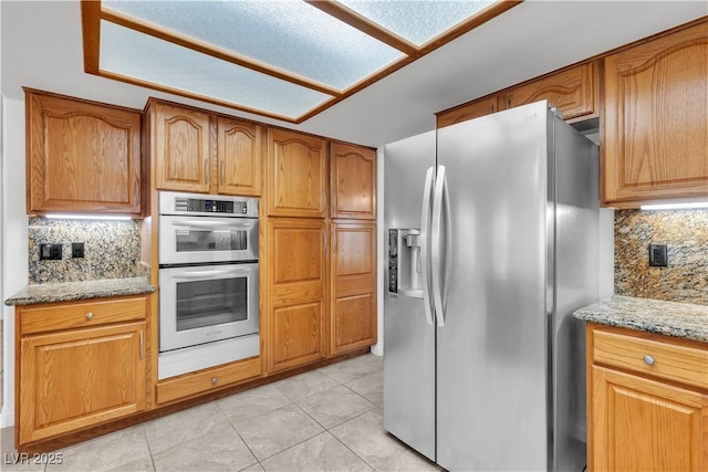8437 Apple Hill Ct, Las Vegas, NV 89128 - kitchen featuring appliances with stainless steel finishes, light stone counters, backsplash, light tile patterned floors, and brown cabinets