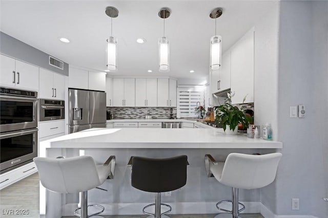 5125 Turnberry Ln, Las Vegas, NV 89113 - kitchen with appliances with stainless steel finishes, a peninsula, light countertops, a kitchen bar, and decorative backsplash