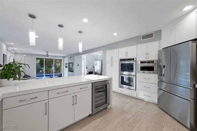5125 Turnberry Ln, Las Vegas, NV 89113 - kitchen with stainless steel appliances, wine cooler, white cabinets, light countertops, and decorative light fixtures