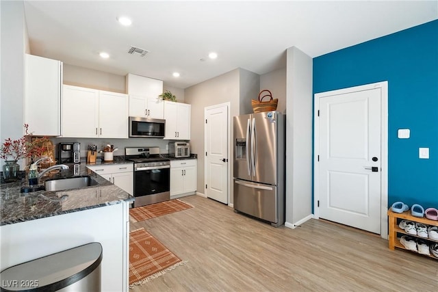 1023 Brilliant Meadow Ave, North Las Vegas, NV 89086 - kitchen with stainless steel appliances, a sink, dark stone countertops, light wood-style floors, and white cabinetry