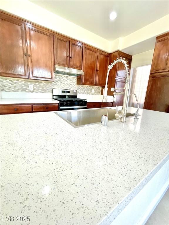 8397 San Ramon Dr, Las Vegas, NV 89147 - kitchen featuring stainless steel range with gas cooktop, under cabinet range hood, light stone countertops, and decorative backsplash