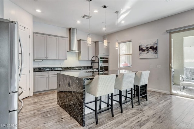 kitchen with appliances with stainless steel finishes, gray cabinets, wall chimney exhaust hood, light wood finished floors, and recessed lighting