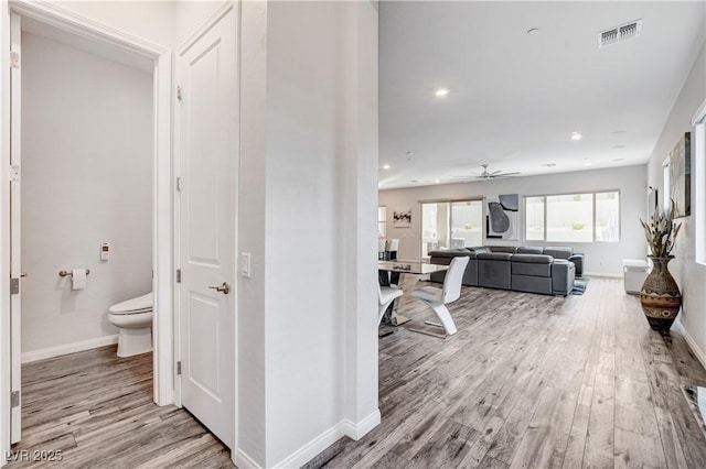 hallway featuring light wood finished floors, baseboards, and recessed lighting