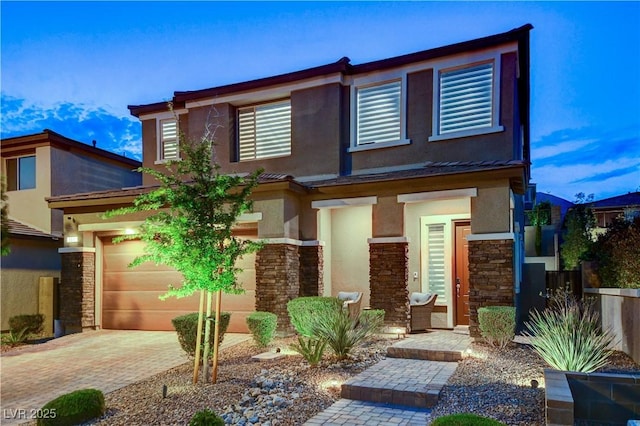 view of front of home featuring stone siding, stucco siding, decorative driveway, and fence