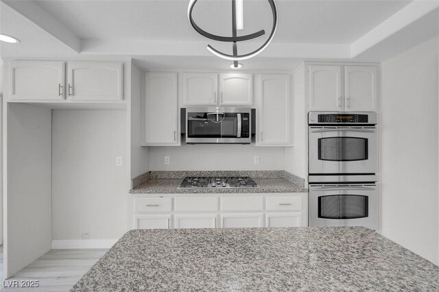 3604 N Campbell Rd, Las Vegas, NV 89129 - kitchen with stainless steel appliances, light stone countertops, white cabinets, light wood-style floors, and baseboards
