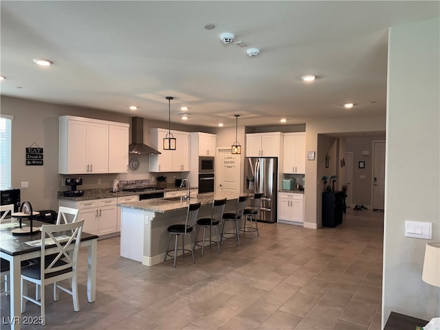 7855 Skyler Falls Ln, North Las Vegas, NV 89084 - kitchen featuring wall chimney range hood, appliances with stainless steel finishes, a kitchen bar, white cabinets, and a kitchen island with sink