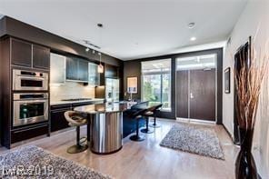 8925 W Flamingo Rd Unit 117, Las Vegas, NV 89147 - kitchen with light wood-style flooring, a breakfast bar area, tasteful backsplash, stainless steel double oven, and recessed lighting