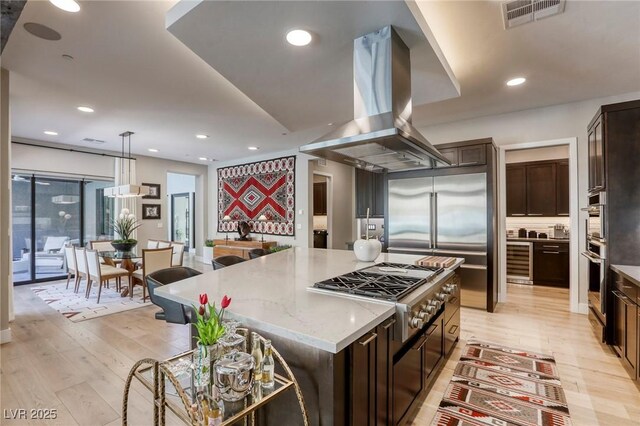 787 Keyland St, Las Vegas, NV 89138 - kitchen with island exhaust hood, stainless steel appliances, light stone counters, light wood-style flooring, and dark brown cabinetry