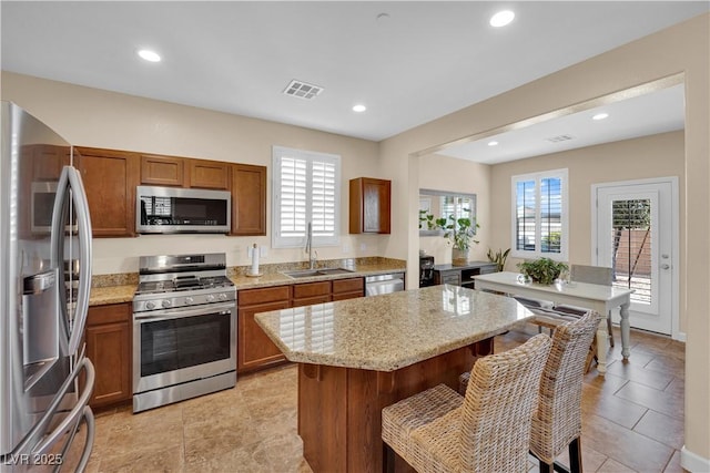 1104 Aspen Cliff Dr, Henderson, NV 89011 - kitchen with appliances with stainless steel finishes, a sink, brown cabinets, light stone counters, and a breakfast bar