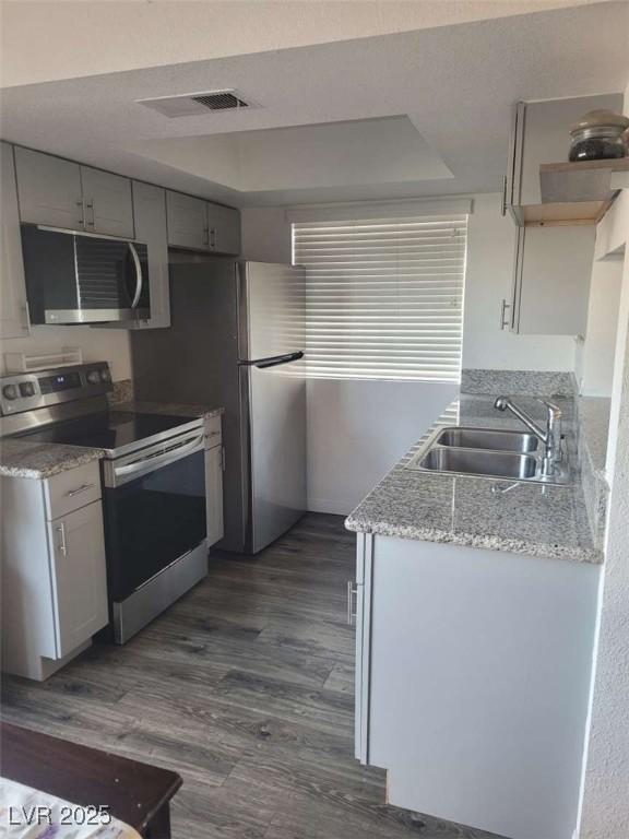5335 Rod Ct Unit 102, Las Vegas, NV 89122 - kitchen featuring appliances with stainless steel finishes, a sink, a raised ceiling, dark wood-style flooring, and gray cabinetry