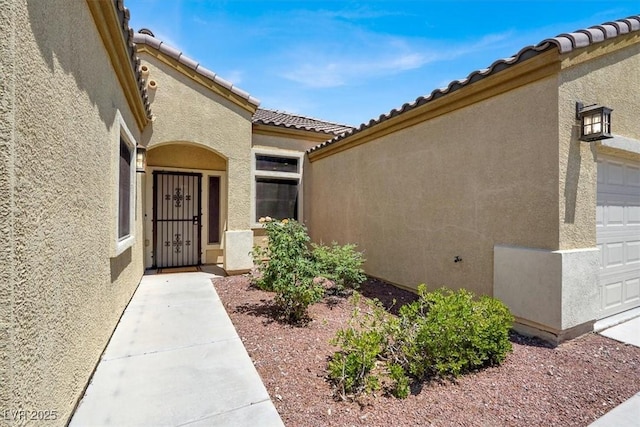 1212 E Rome Blvd, North Las Vegas, NV 89086 - view of exterior entry with stucco siding, a tile roof, and a garage