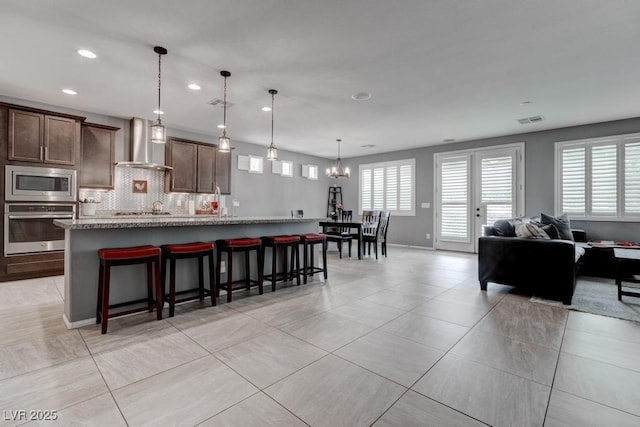 6985 Hopi Summit Ct, Las Vegas, NV 89149 - kitchen with appliances with stainless steel finishes, wall chimney exhaust hood, recessed lighting, a breakfast bar, and decorative backsplash
