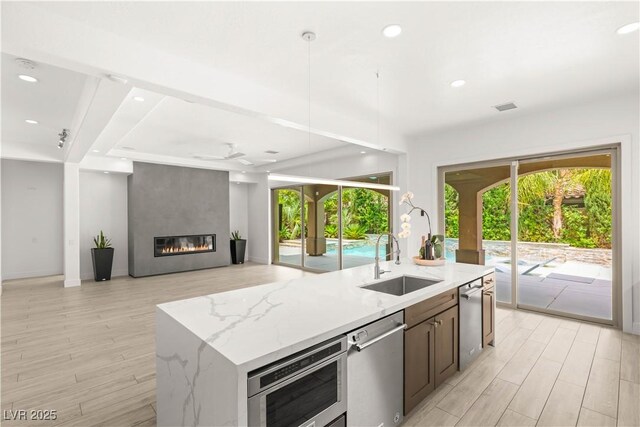 2240 Boutique Ave, Henderson, NV 89044 - kitchen featuring a sink, stainless steel dishwasher, light wood-style floors, a kitchen island with sink, and healthy amount of natural light