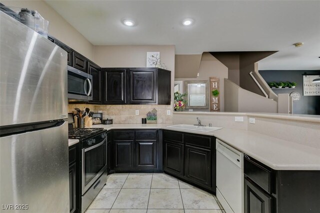 5509 Ante Up Ct Unit 102, Las Vegas, NV 89122 - kitchen with appliances with stainless steel finishes, dark cabinets, a sink, a peninsula, and decorative backsplash
