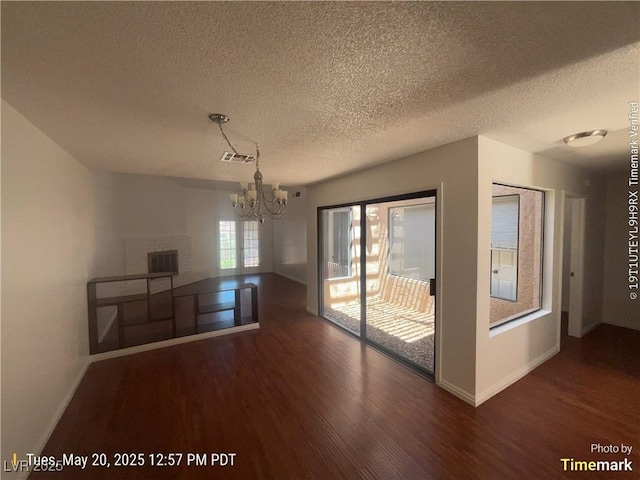 unfurnished dining area featuring wood finished floors, a textured ceiling, a chandelier, and baseboards