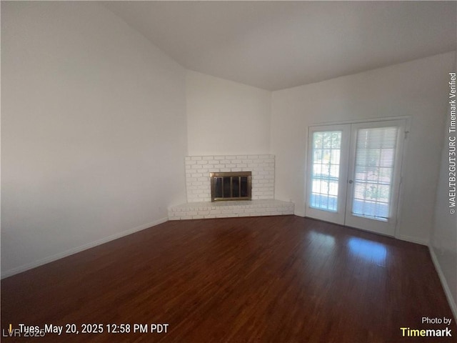 unfurnished living room with wood finished floors, baseboards, a fireplace, french doors, and lofted ceiling