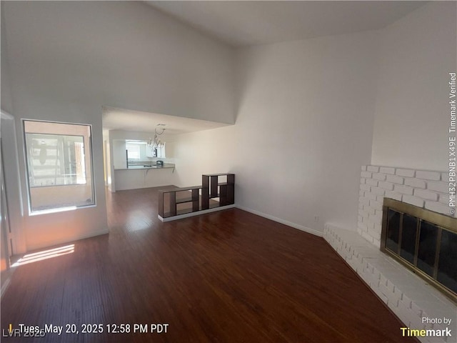 unfurnished living room with wood finished floors, a fireplace, a chandelier, and baseboards