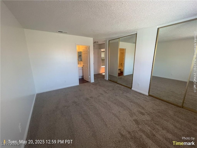 unfurnished bedroom with multiple closets, carpet, a textured ceiling, baseboards, and ensuite bathroom
