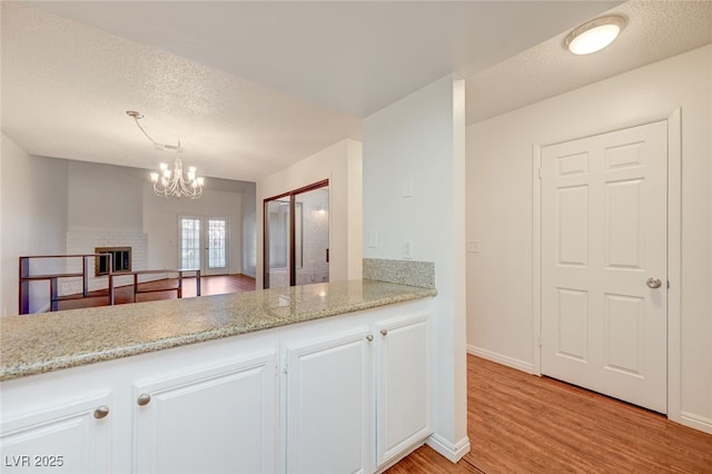 1850 Camino Verde Ln, Las Vegas, NV 89119 - kitchen featuring light wood-type flooring, white cabinets, a textured ceiling, a chandelier, and light stone counters