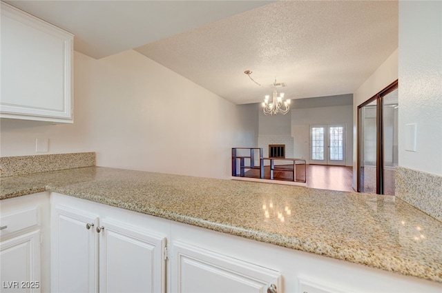 1850 Camino Verde Ln, Las Vegas, NV 89119 - kitchen featuring white cabinetry, a chandelier, a brick fireplace, light stone counters, and a textured ceiling