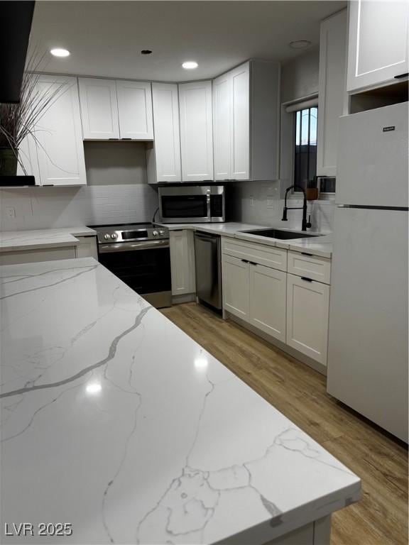 150 Greenbriar Townhouse Way, Las Vegas, NV 89121 - kitchen featuring stainless steel appliances, a sink, decorative backsplash, white cabinetry, and light wood finished floors