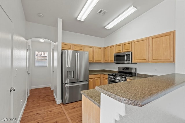 2596 Lazy Saddle Dr, Henderson, NV 89002 - kitchen featuring stainless steel appliances, vaulted ceiling, light wood-style floors, a peninsula, and light brown cabinets