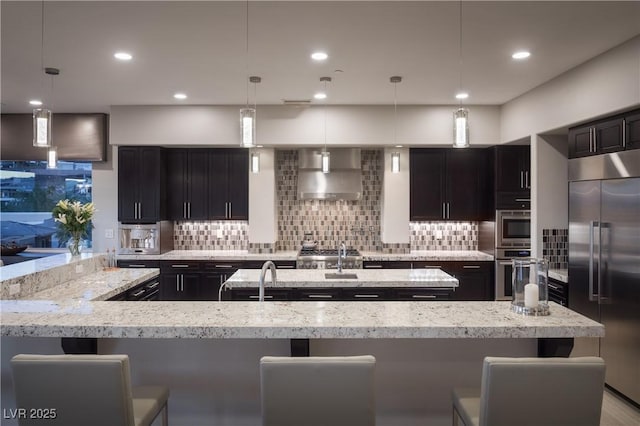 1683 Tangiers Dr, Henderson, NV 89012 - kitchen with built in appliances, wall chimney range hood, tasteful backsplash, light stone countertops, and recessed lighting
