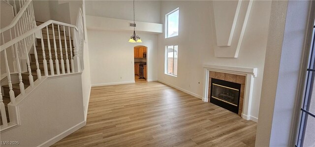 3750 Morning Canyon St, Las Vegas, NV 89147 - unfurnished living room with light wood-style flooring, stairs, a tiled fireplace, baseboards, and a high ceiling