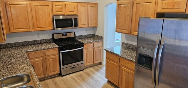 3750 Morning Canyon St, Las Vegas, NV 89147 - kitchen with stainless steel appliances, light wood finished floors, dark stone counters, and arched walkways