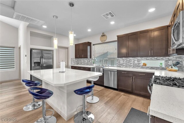8076 Haywood Estate Ave, Las Vegas, NV 89113 - kitchen with appliances with stainless steel finishes, a kitchen bar, dark brown cabinetry, light wood-type flooring, and decorative backsplash