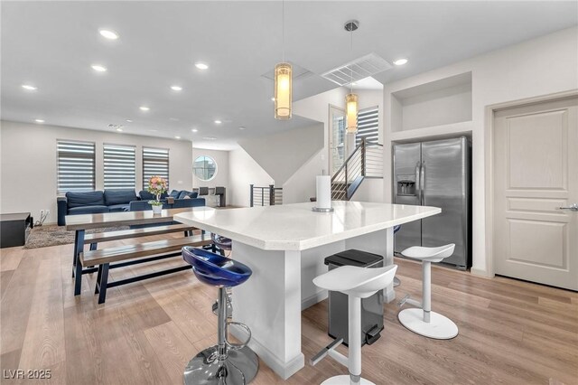 8076 Haywood Estate Ave, Las Vegas, NV 89113 - kitchen with stainless steel fridge with ice dispenser, light wood-style floors, a breakfast bar, light countertops, and recessed lighting
