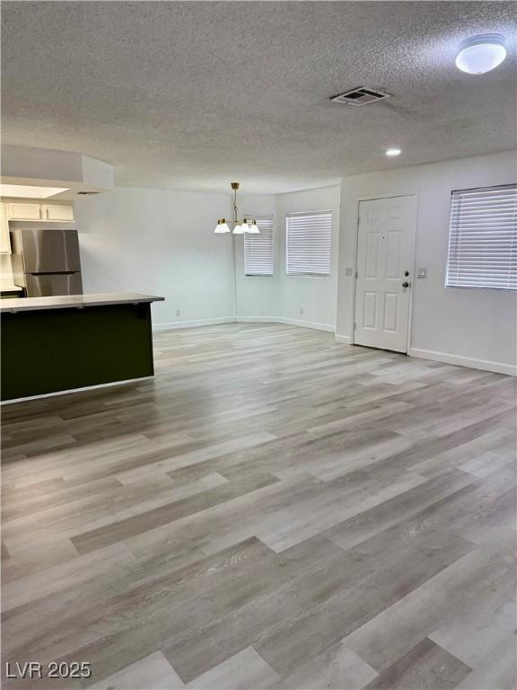 1320 Driscoll Dr Unit 202, Las Vegas, NV 89128 - unfurnished living room with a chandelier, a textured ceiling, light wood-style flooring, and baseboards