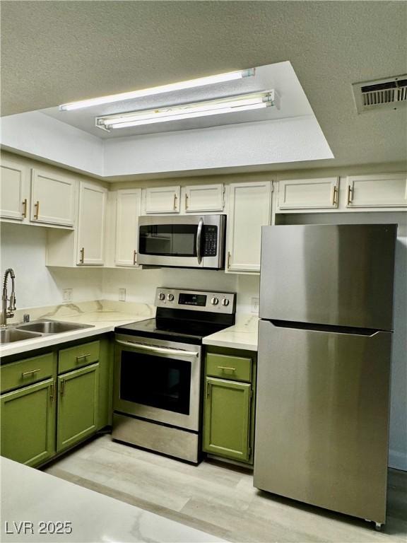 1320 Driscoll Dr Unit 202, Las Vegas, NV 89128 - kitchen featuring appliances with stainless steel finishes, green cabinets, a sink, light wood finished floors, and a textured ceiling