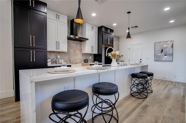 10025 Netherton Dr, Las Vegas, NV 89134 - kitchen featuring wall chimney exhaust hood, a breakfast bar area, tasteful backsplash, light wood-style flooring, and a kitchen island with sink
