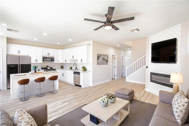 6387 Azurelyn Ave, Las Vegas, NV 89122 - living room featuring light wood finished floors, a ceiling fan, a large fireplace, stairs, and baseboards