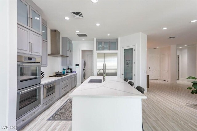271 E Shelbourne Ave, Las Vegas, NV 89123 - kitchen with wall chimney exhaust hood, built in appliances, a sink, a center island with sink, and estacked washer and dryer