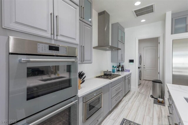 271 E Shelbourne Ave, Las Vegas, NV 89123 - kitchen with wall chimney exhaust hood, stacked washing machine and dryer, stainless steel appliances, light countertops, and gray cabinets