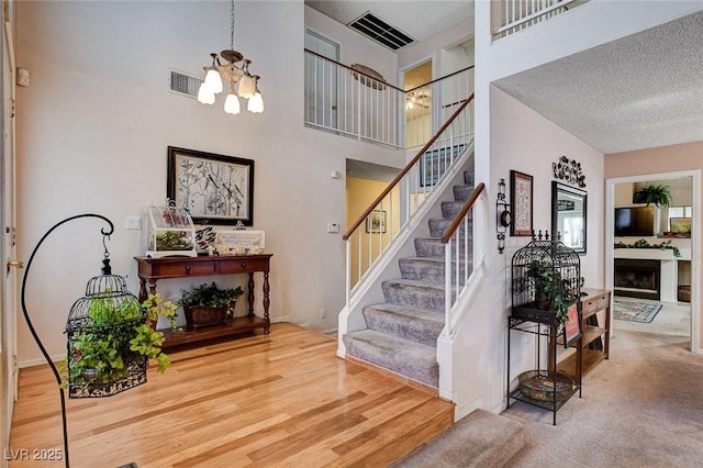 7109 Deepriver Cir, Las Vegas, NV 89129 - stairs featuring a chandelier, a textured ceiling, a fireplace, a high ceiling, and wood finished floors
